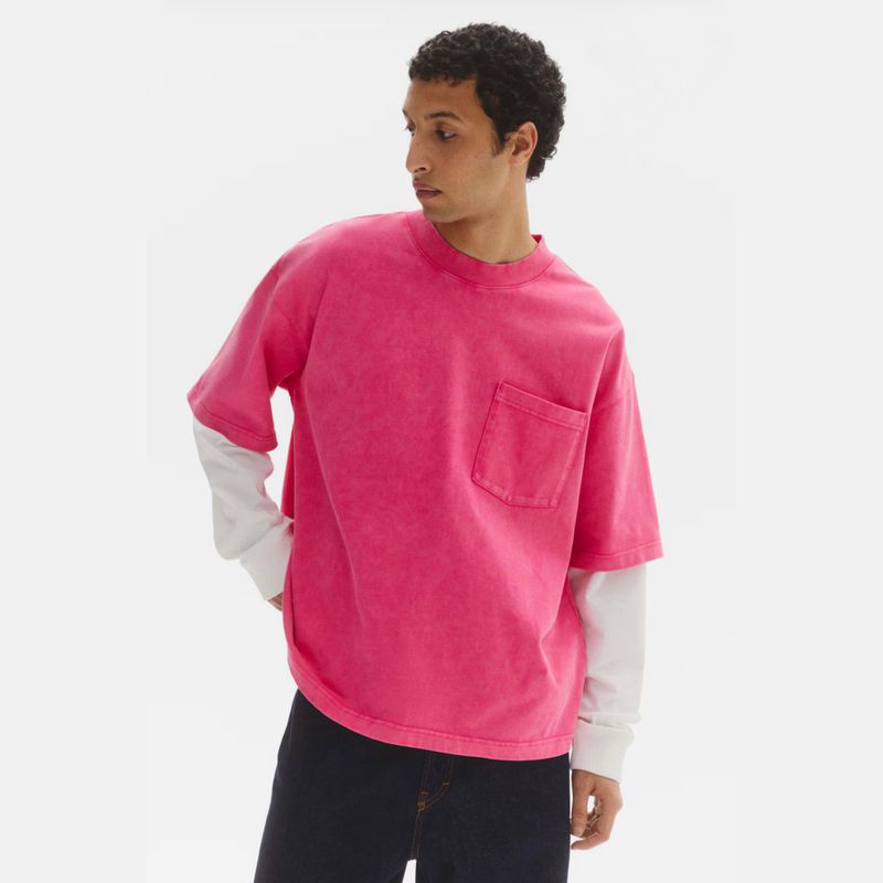Model Anass Bouazzaoui wears a washed bright pink short-sleeve pocket t-shirt over a white long sleeve on a white studio background.