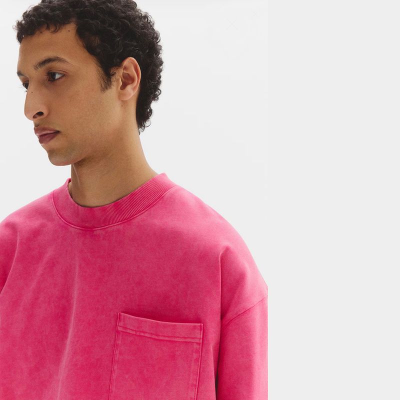 Close-up portrait of a male model wearing a bright pink crewneck t-shirt against a plain white background for H&M Men April 2026 lookbook.
