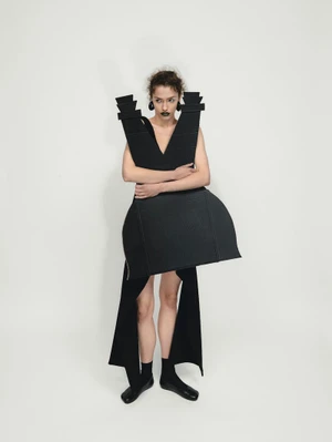 Model wearing sculptural black architectural fashion piece and black lipstick standing against a white seamless background