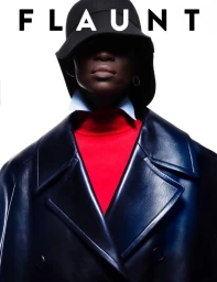 Model Achok wears a black bucket hat, dark leather trench coat, and bright red turtleneck against a white background for Flaunt.