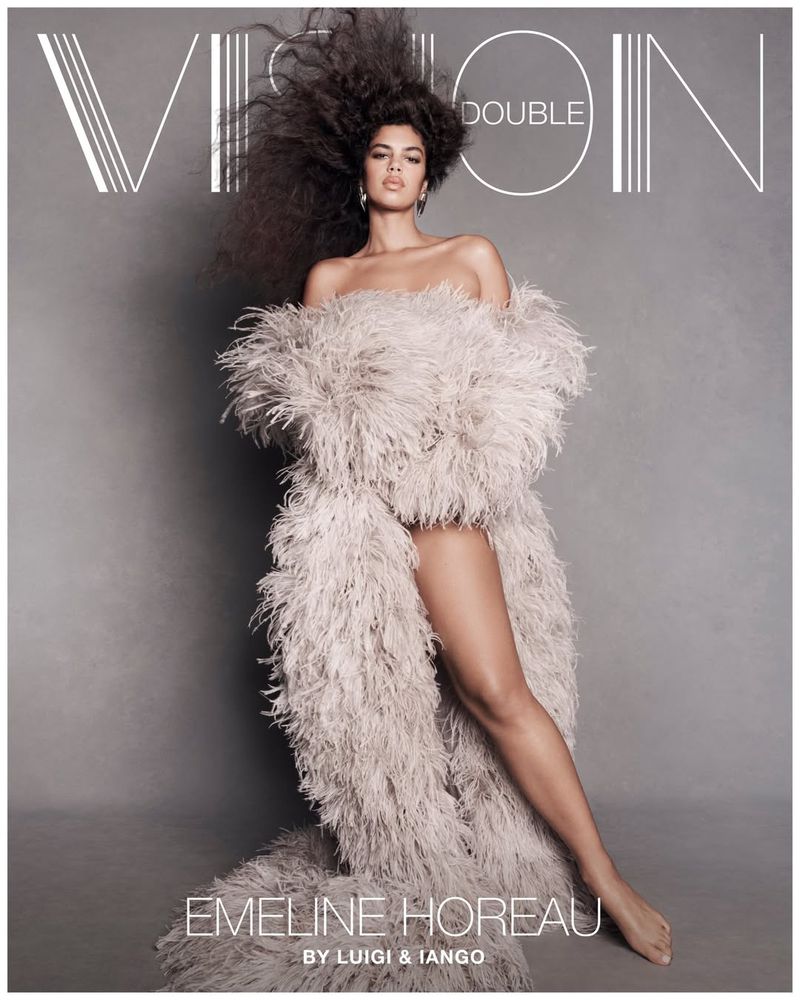 Model Emeline Hoareau posing barefoot in a voluminous grey feather coat against a studio backdrop for Double Vision.