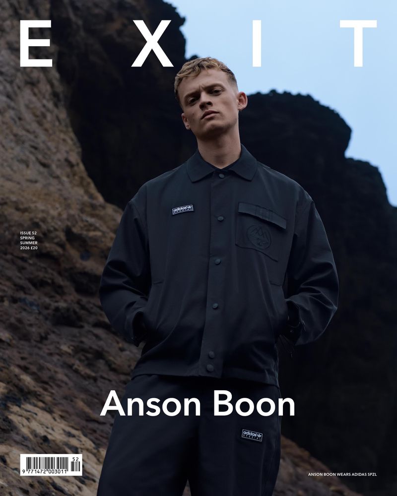 Actor Anson Boon wearing a dark collared jacket and matching trousers outdoors against rugged rocks on the cover of Exit Magazine.