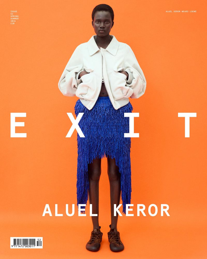 Model Aluel Keror stands against an orange backdrop wearing an off-white jacket and a textured royal blue fringe skirt.