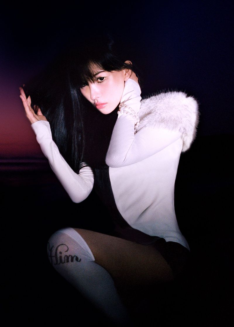 East Asian woman posing in a white fur-trimmed long-sleeve top and knee-high socks against a dark twilight sky.