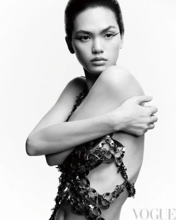 Monochrome portrait of an Asian woman wearing a metallic garment, striking a pose against a stark white background in a studio setting.