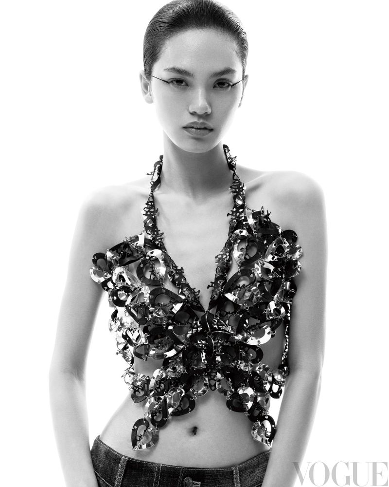Monochrome portrait of a model in a butterfly-shaped jewel top and dark jeans against a bright white backdrop, posing in a studio.