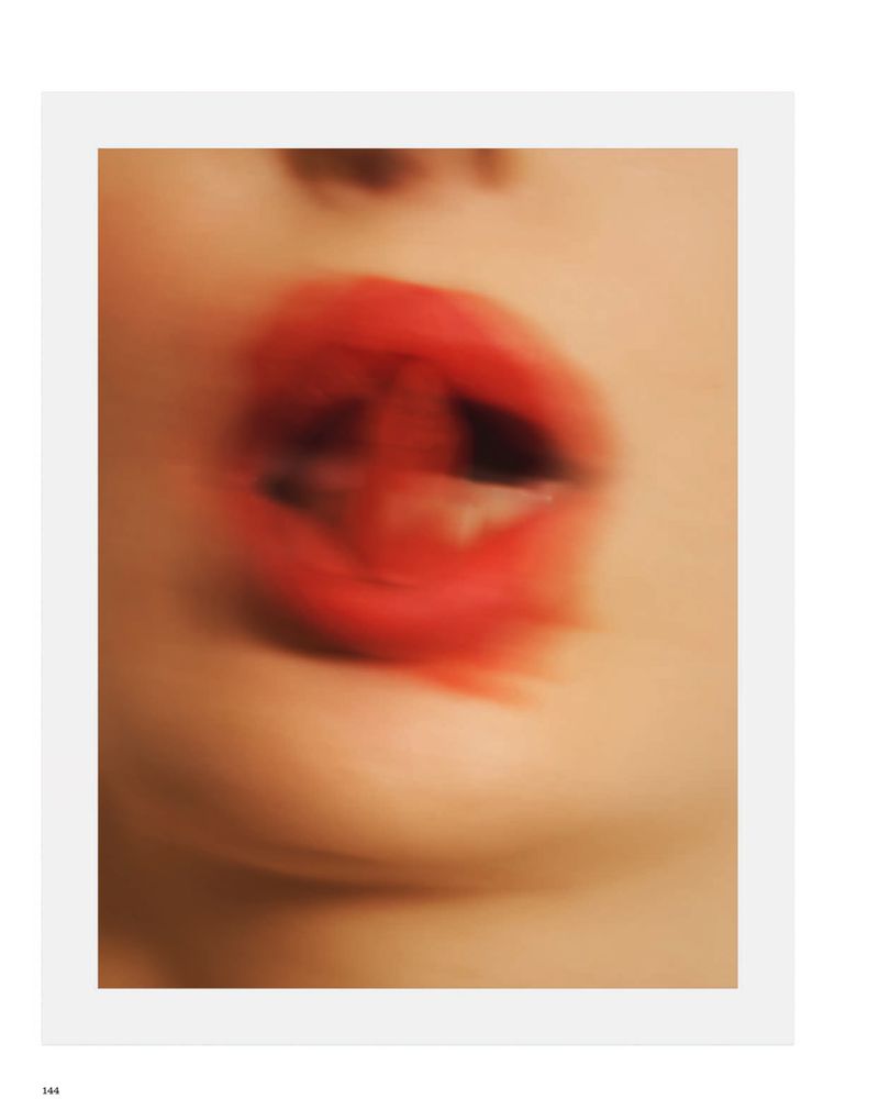 Motion-blurred close-up of open lips wearing bright red lipstick against pale skin in a beauty editorial.