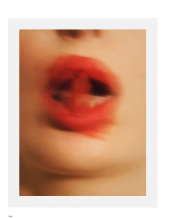 Motion-blurred close-up of open lips wearing bright red lipstick against pale skin in a beauty editorial.