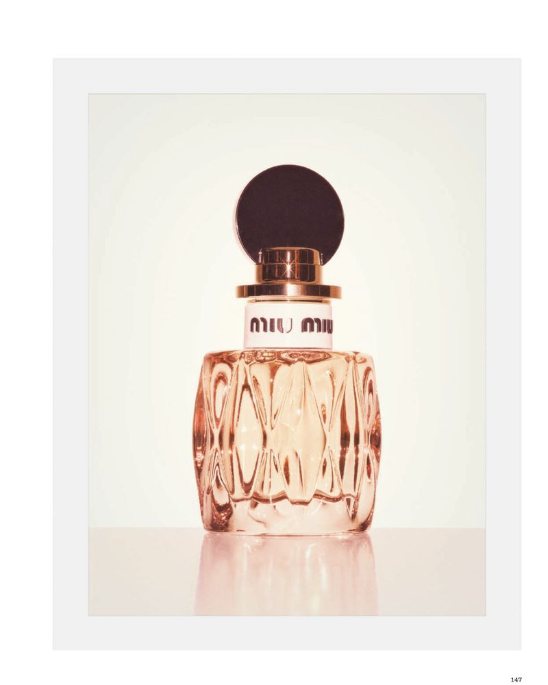 Miu Miu glass perfume bottle with a round black cap and gold collar standing on a reflective white surface.