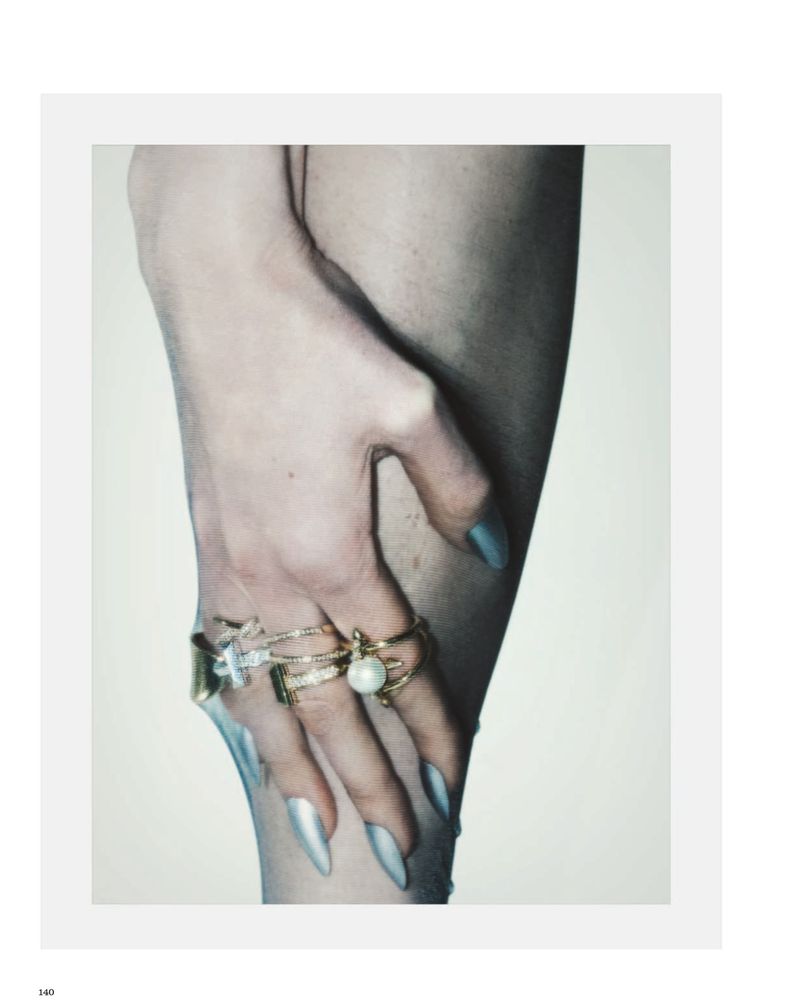 Close-up of a hand with silver pointed manicured nails wearing stacked gold, diamond, and pearl rings against skin.