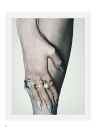 Close-up of a hand with silver pointed manicured nails wearing stacked gold, diamond, and pearl rings against skin.