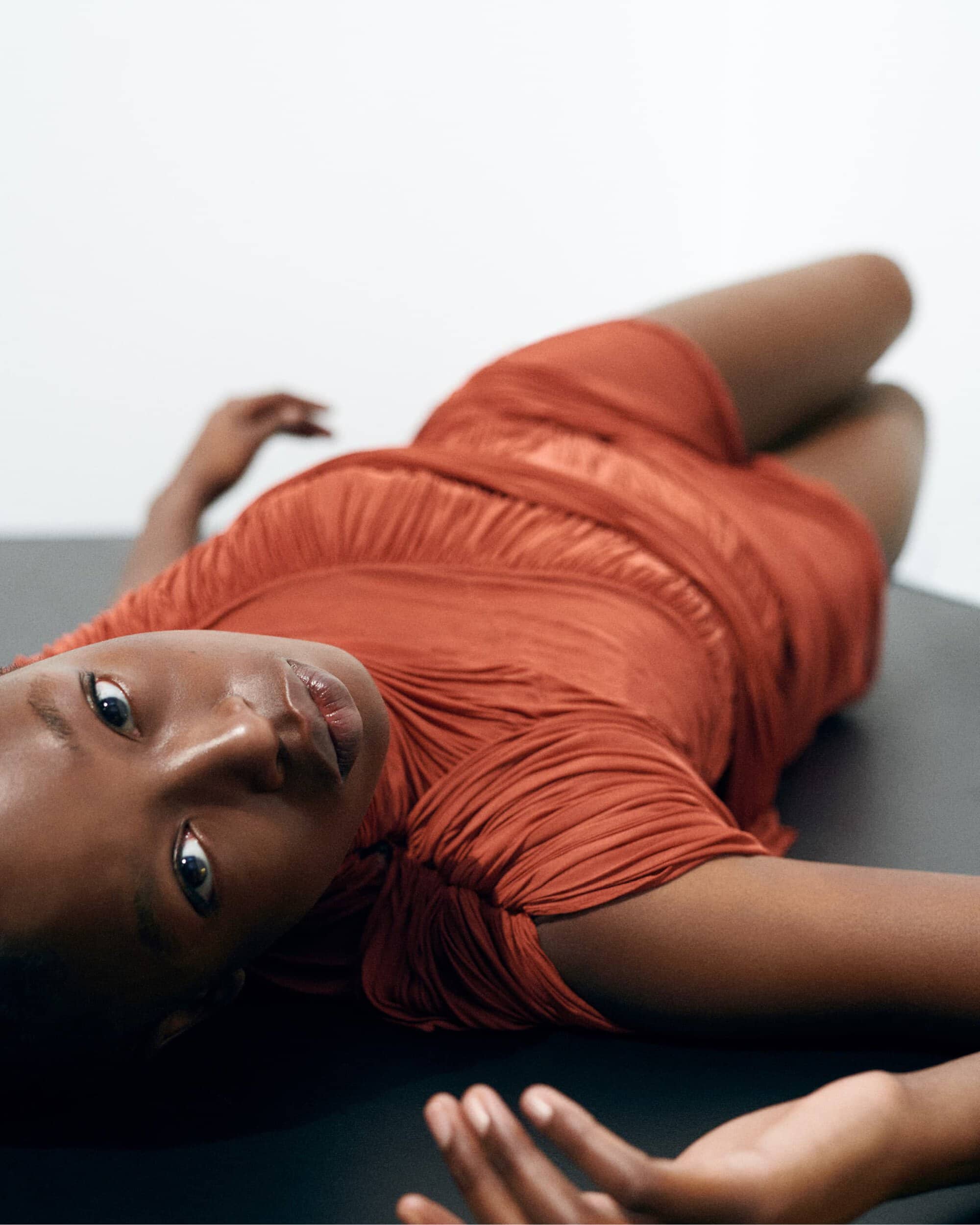 Model lying on a dark surface in a rust-colored dress for Balmain spring 2026 ad campaign