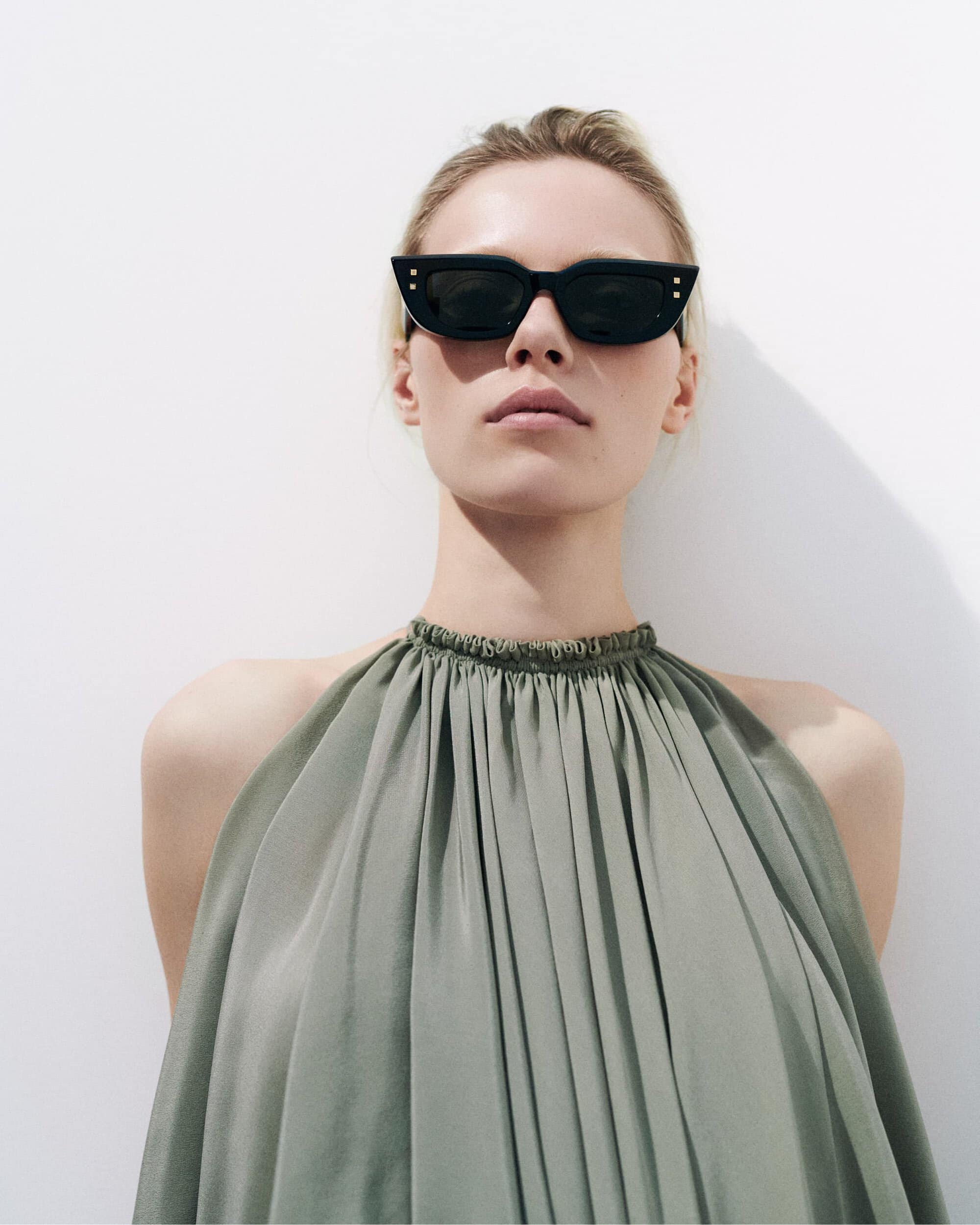 Model wearing dark sunglasses and a gathered green halter top against a plain white background for Balmain