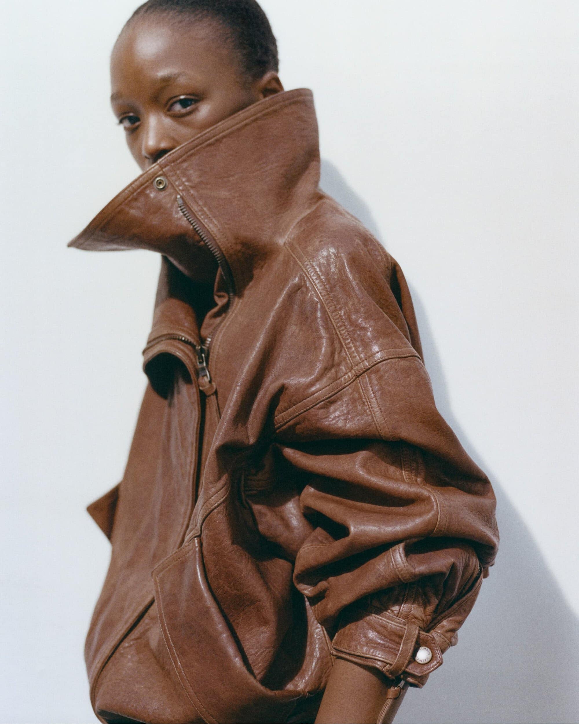 Model wearing an oversized brown leather jacket with a high structured collar against a plain white background.