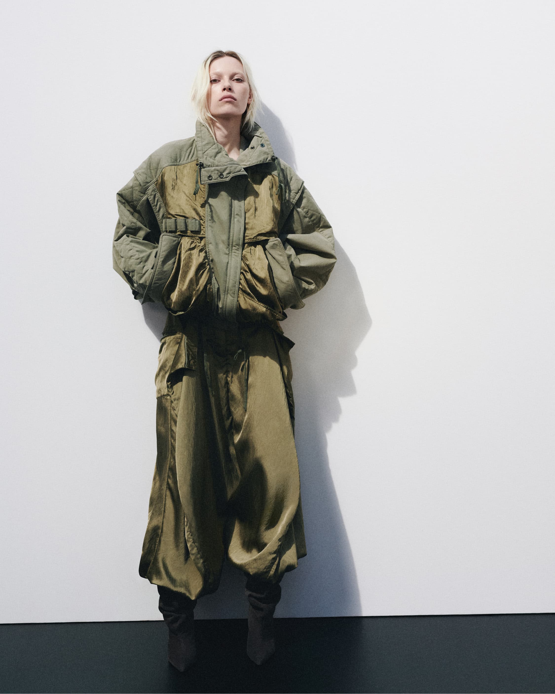 Model in an olive green quilted jacket and matching trousers standing against a plain white studio background.