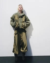 Model in an olive green quilted jacket and matching trousers standing against a plain white studio background.
