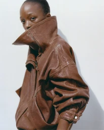 Model wearing an oversized brown leather jacket with a high structured collar against a plain white background.