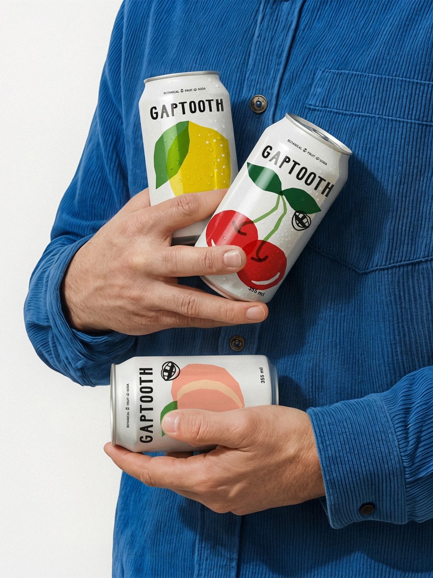 Person wearing a blue corduroy shirt holding three Gaptooth beverage cans featuring lemon, cherry, and peach illustrations.