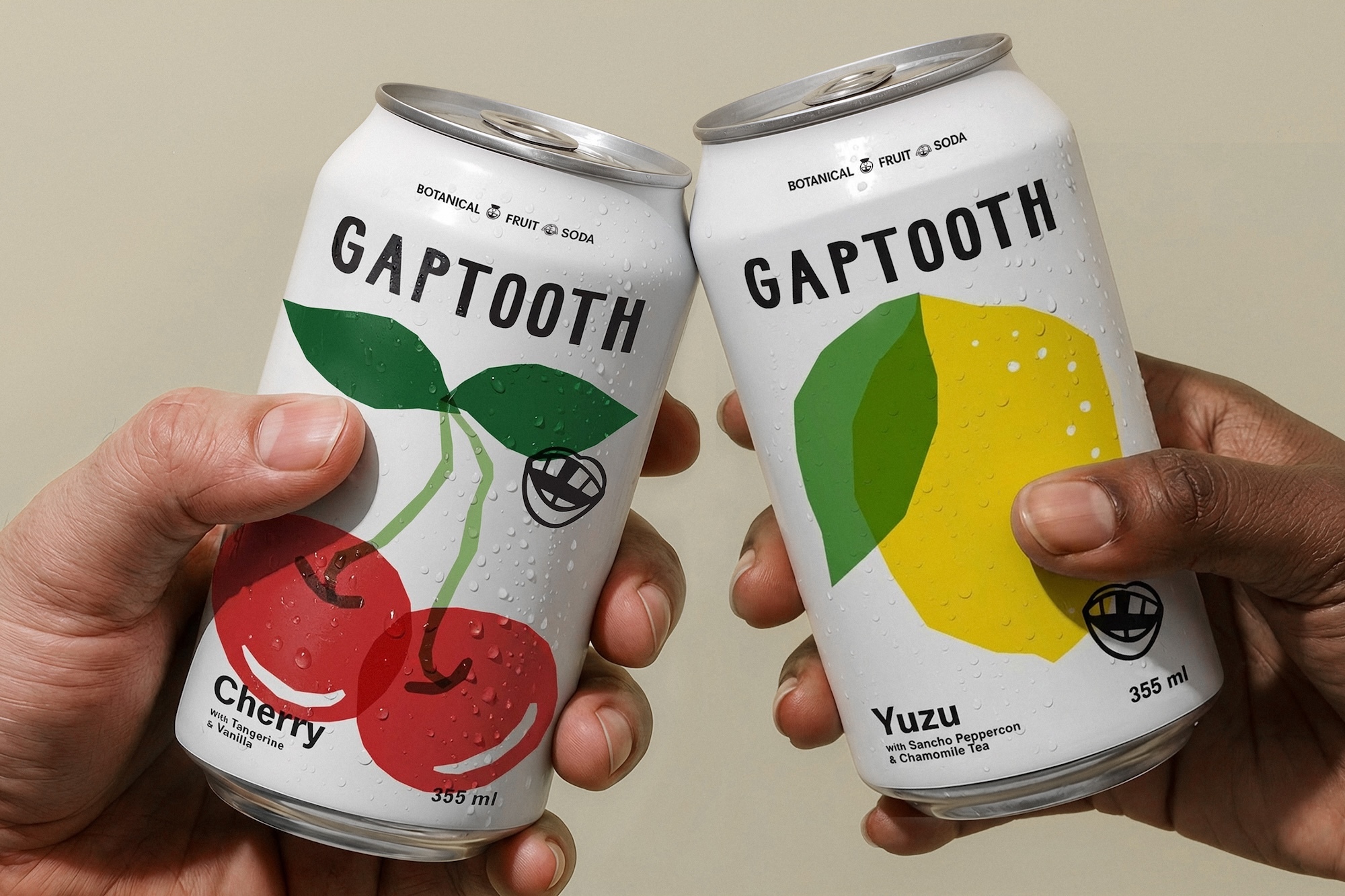 Two hands holding up chilled Gaptooth beverage cans featuring cherry and yuzu fruit illustrations against a plain background