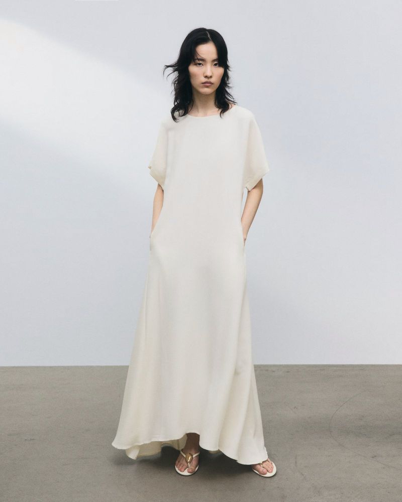 Model wearing a long white short-sleeve maxi dress standing against a plain studio background.