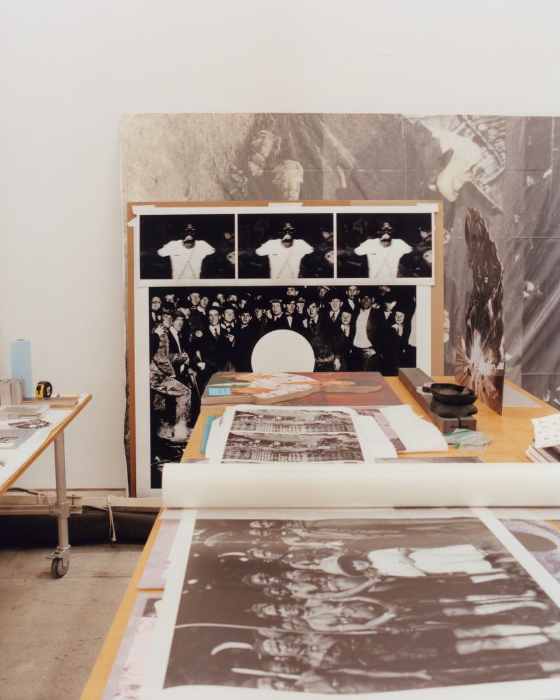 Interior studio shot showing large black-and-white photographic prints and art boards laid out across wooden work tables for Arthur Jafa.