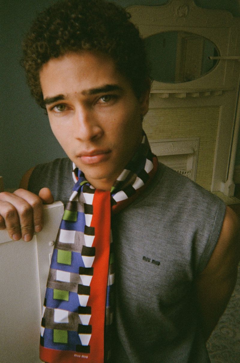 Close-up portrait of a man with curly hair wearing a grey sleeveless top and a colorful patterned scarf.