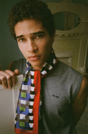 Close-up portrait of a man with curly hair wearing a grey sleeveless top and a colorful patterned scarf.