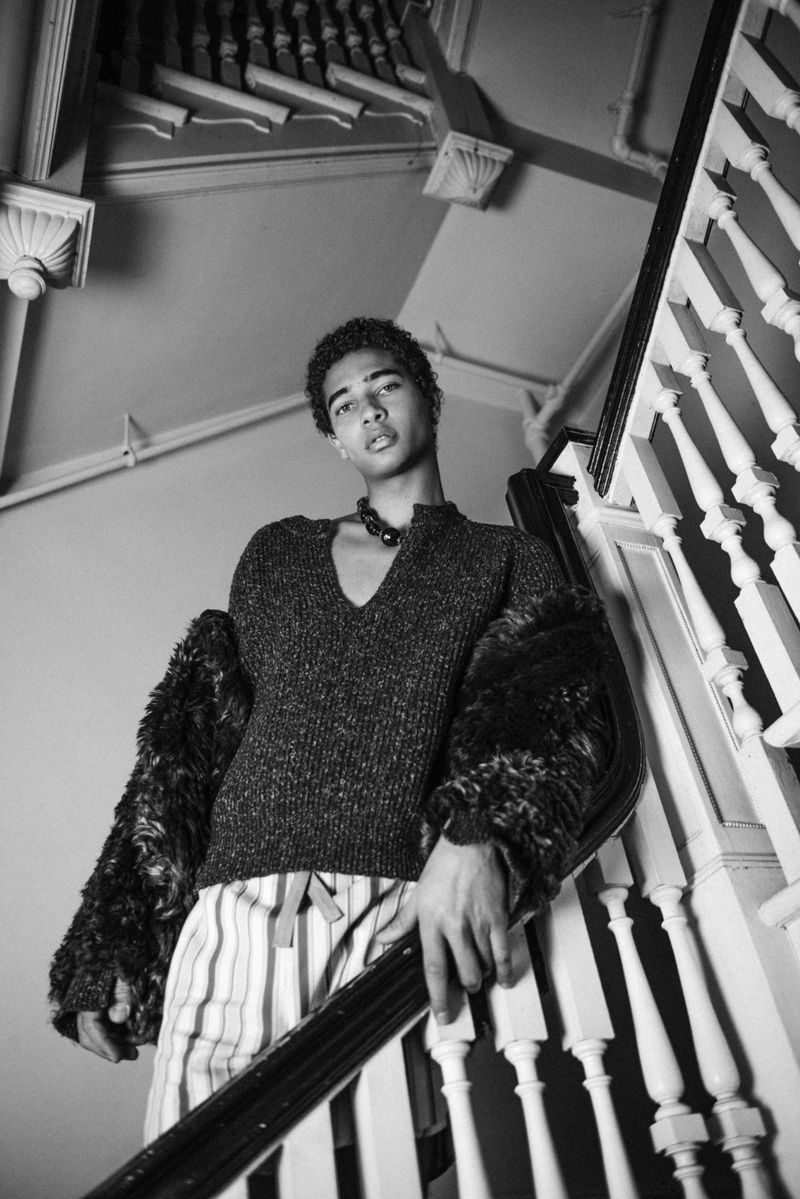 Monochrome low-angle portrait of a young man wearing a dark V-neck sweater and patterned trousers on a staircase