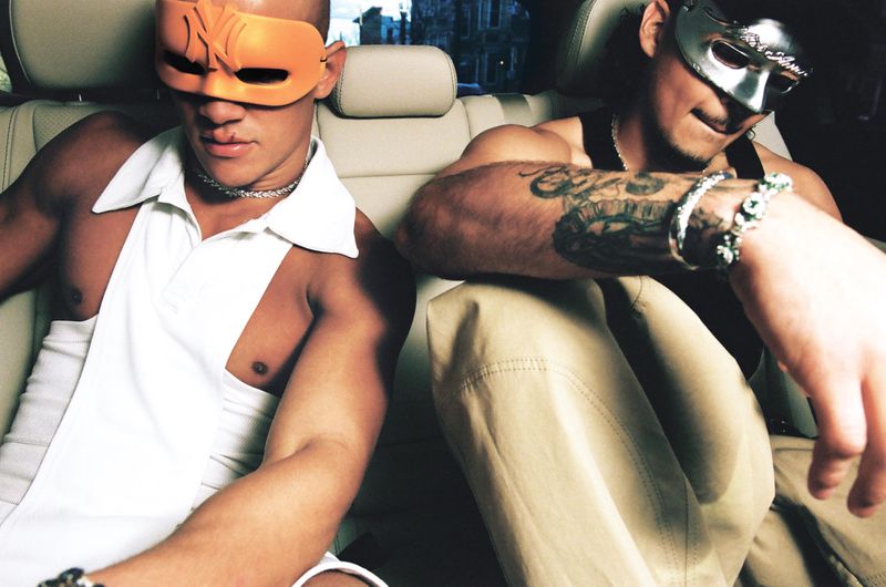Two men seated in the back of a car wearing masks and casual clothing in an editorial portrait for i-D Magazine.