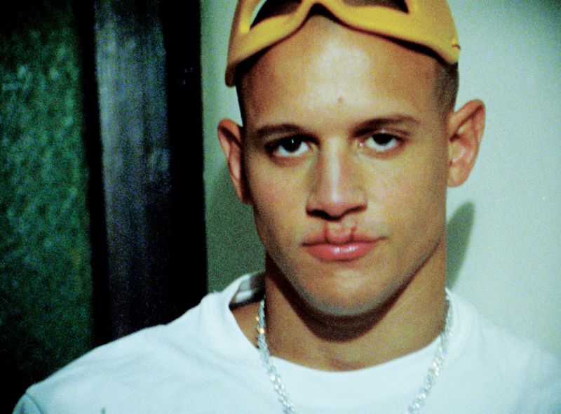 Close-up portrait of Saul Rodriguez wearing a white t-shirt and yellow glasses on his head for i-D Magazine
