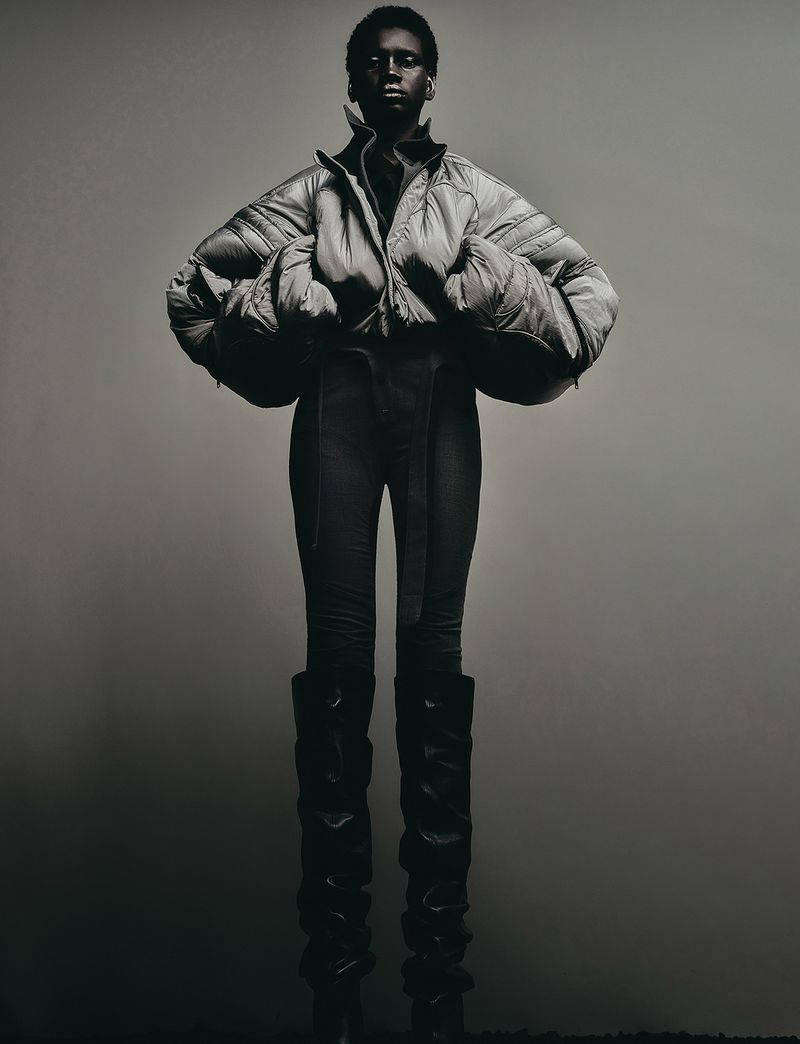 Model wearing a voluminous puffer jacket and tall boots against a plain gradient background for Numero Netherlands.