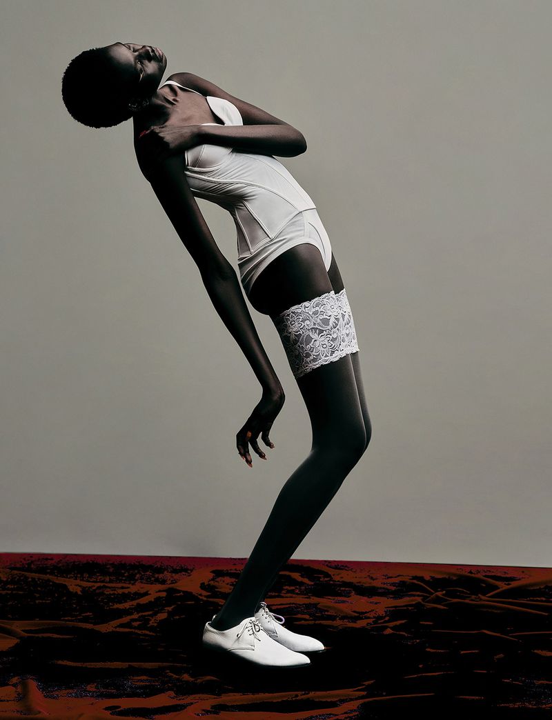 Model Nyagoa Diu arching backward wearing white lingerie body suit and white shoes against grey studio backdrop