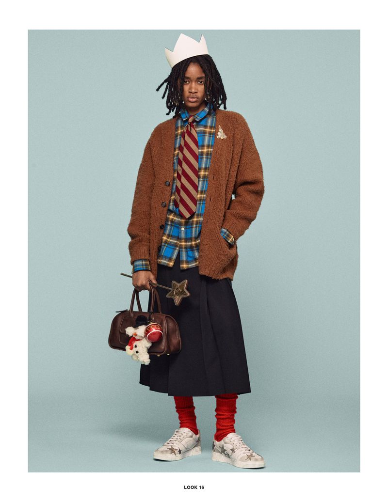 Adult wearing a brown cardigan, plaid shirt, skirt, sneakers and a paper crown, holding a handbag and a magic wand, on a blue background.