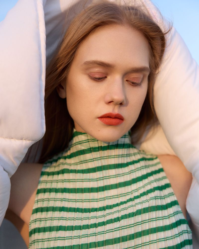 Close-up portrait of a woman wearing a green and white striped top framed by white quilted fabric.