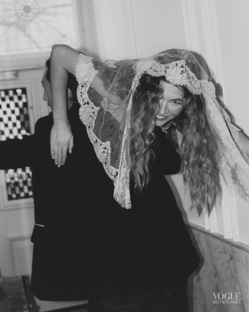 Woman in lace veil is carried by a man in a suit in a black and white Vogue Netherlands fashion editorial image.
