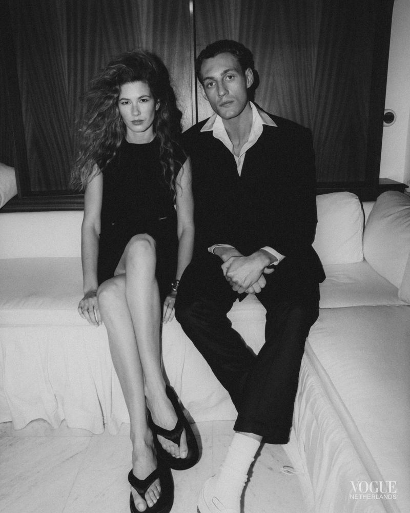 Black and white portrait of a man and woman seated together on a white sofa for Vogue Netherlands