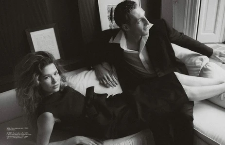 Black and white editorial portrait of a woman reclining and a man seated on a light couch in a room.