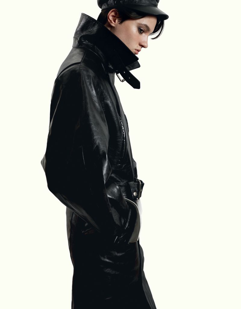 Model wearing a black leather coat and cap against a solid white background for HERO Magazine