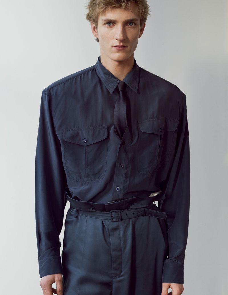 A male model wearing a dark navy buttoned shirt and matching trousers against a plain neutral background.