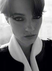 Close-up monochrome portrait of a model with dark short hair and heavy eye makeup wearing a white and black collared top