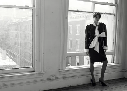 Model standing by large windows wearing a dark jacket with a white bow tie for HERO Magazine