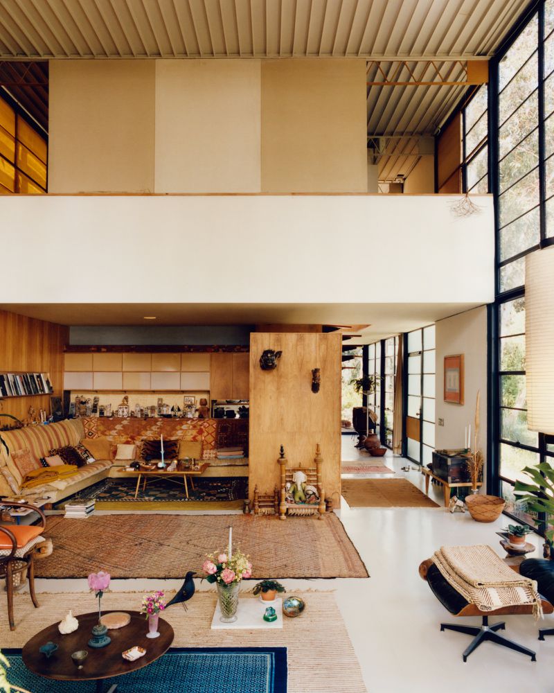 Spacious mid-century modern interior features high ceilings, large windows, and eclectic decor, with a living area and upper level.