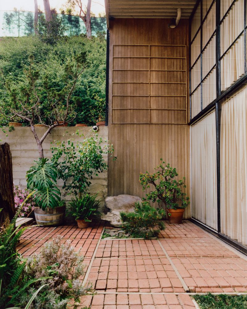 Exterior courtyard of the Eames House with red brick paving, potted plants, and wood paneling shot by Keith Oshiro