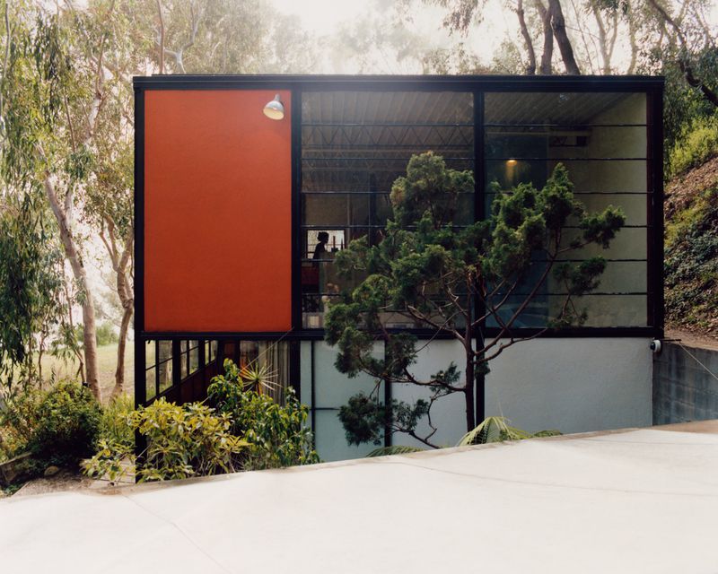 Exterior view of The Eames House with vibrant orange paneling and large glass windows surrounded by eucalyptus trees.