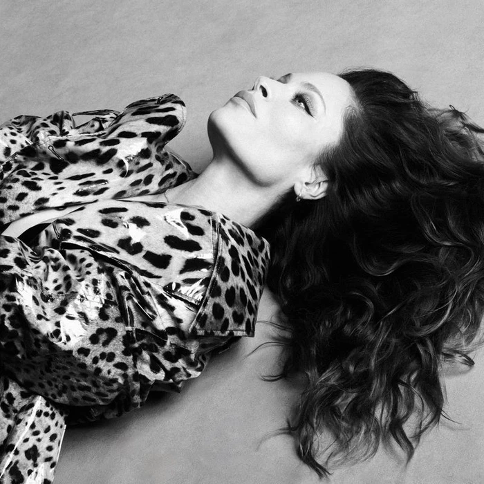 Model Frankie Rayder wearing a leopard print coat lying down against a plain studio background in a black and white fashion portrait.