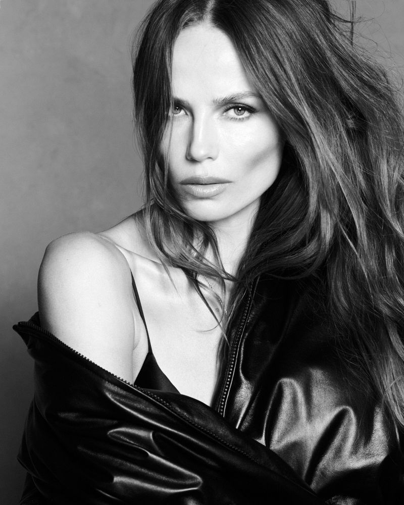 Model Natasha Poly posing in a black leather jacket against a plain grey studio backdrop in a black and white portrait.