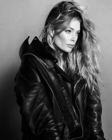 Model Doutzen Kroes in a black leather jacket against a plain grey background, photographed in black and white.