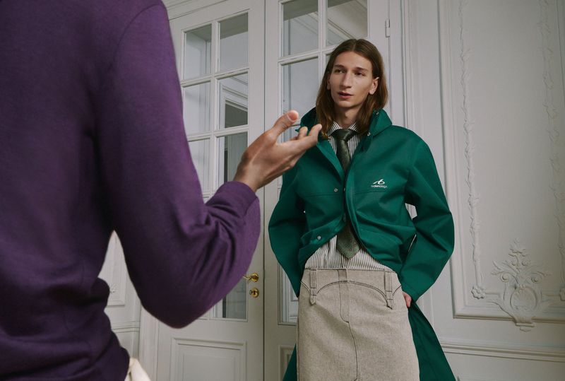 Model wearing a green coat and patterned tie standing in an interior space with white panelled double doors