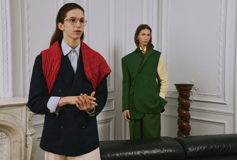 Two male models posing indoors in front of ornate white walls, wearing layered tailored menswear for AnOther Man Magazine.