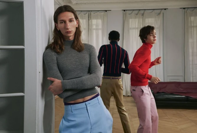 Group of male models in an interior setting wearing a grey turtleneck and light blue trousers
